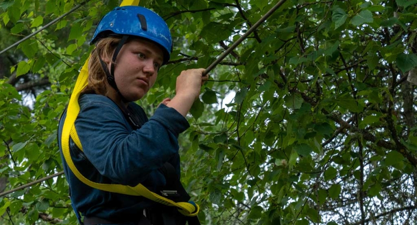 A person wearing safety gear navigates a high ropes course